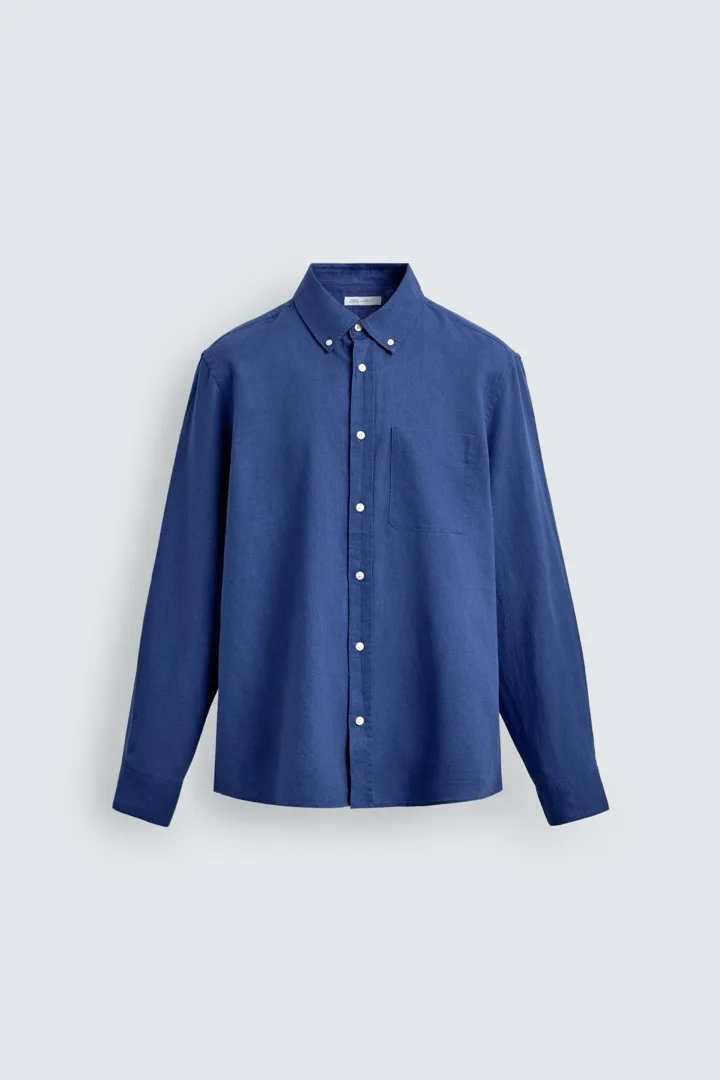 Indigo linen button-up shirt on a wooden hanger over a white tee against a light background